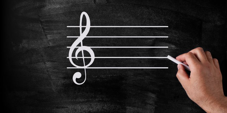 Eine Hand zeichnet mit Kreide ein Notensystem und einen Violinschlüssel auf eine Tafel.