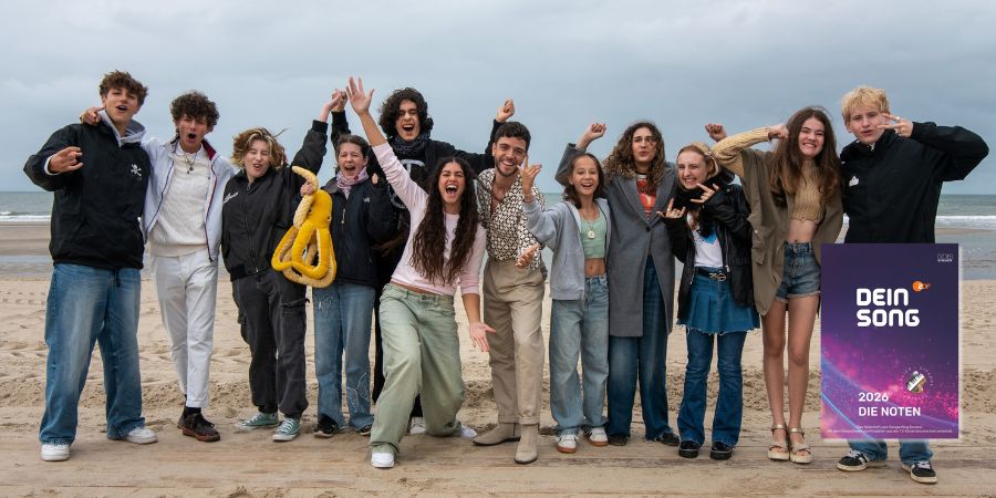 Gruppe von jugendlichen Teilnehmerinnen und Teilnehmern der KiKA-Show „Dein Song“ 2026 steht gemeinsam am Strand und jubelt in die Kamera. Die jungen Songwriter:innen lachen, springen und posieren vor dem Meer; rechts unten ist das Cover der Notenausgabe „Dein Song 2026 – Die Noten“ eingeblendet.