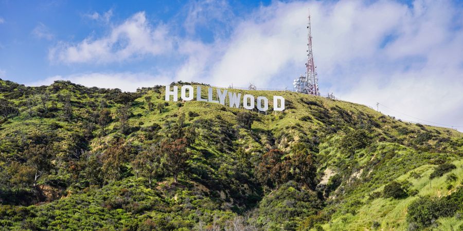 Blick auf das weltbekannte Hollywood-Sign in Los Angeles, auf einem grünen Hügel mit blauem Himmel.
