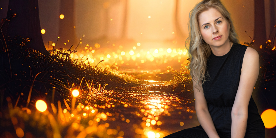 Estonian composer Elis Hallik, with light blonde wavy hair and wearing a sleeveless black top, sits in front of a glowing, mystical forest path at night, surrounded by golden lights.