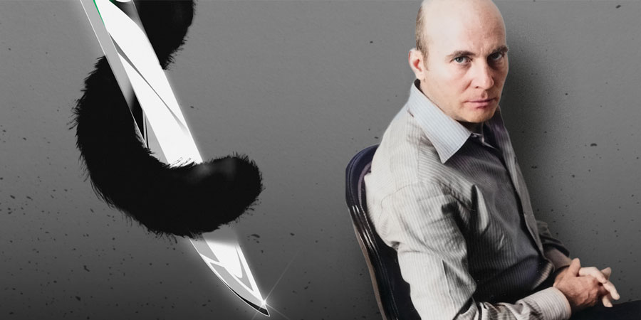 Composer Hans Werner Henze sits on a chair with his hands folded, looking seriously and slightly upward into the camera. In the background on the left side of the image is a stylized dagger with the tail of a black cat wrapped around it.