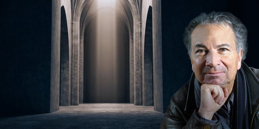 Breiter, dunkler Kirchenraum mit hohen, spitzbogigen Arkaden. In der Mitte fällt ein senkrechter Lichtschein auf den Boden. Rechts im Bildrand sitzt eine Person im Vordergrund, Gesicht unscharf, Hand an das Kinn gelegt.