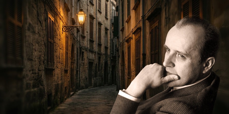Nächtliche, enge Straße mit hohen Steinfassaden und warmem Laternenlicht. Rechts im Bild ein angeschnittenes Porträt einer sitzenden Person (Nino Rota) im Vordergrund, die Hand am Kinn.